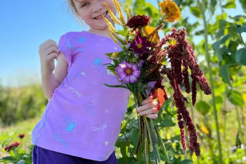 Small girl holding flowers in sunny field